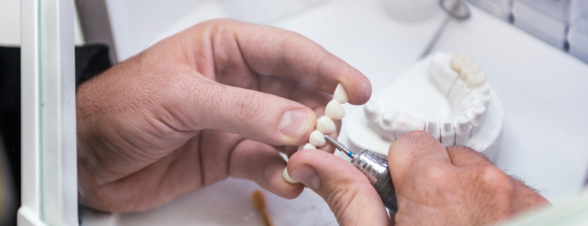 Eine Person bearbeitet Zähne an einem Zahnersatz mit einer Präzisionswerkzeug.